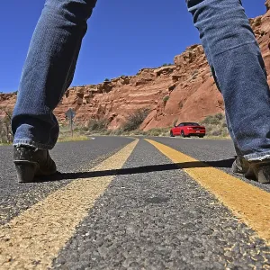 Woman standing in the middle of Route 66 looking at red Ford Mustang convertible