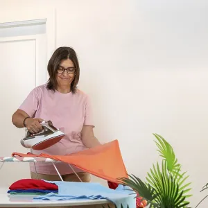 Woman standing smiling while ironing a colorful t shirt on an ironing board