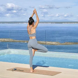 Eine Frau steht in einer Yogahaltung auf dem Dach undblickt über ein ruhiges Meer. Eine Frau steht in einer Yogahaltung auf dem Dach undblickt über ein ruhiges Meer.