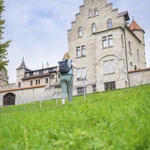 A woman walks up a grassy hill towards an imposing historic castle