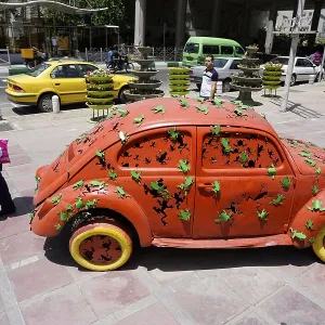 A woman walks past a Volkswagen Beetle art object on the pavement in Tehran