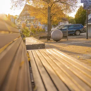 Empty wooden bench in a sunlit village square with half-timbered house in the background Empty wooden bench in a sunlit village square with half-timbered house in the background