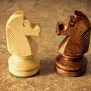 Two wooden knight pieces facing each other on a textured surface