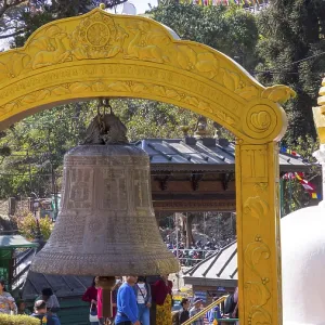A yellow bell tower frames a large bell with a nearby stupa A yellow bell tower frames a large bell with a nearby stupa