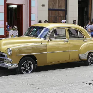 A yellow Chevrolet vintage car stands on an urban street surrounded by historic buildings A yellow Chevrolet vintage car stands on an urban street surrounded by historic buildings
