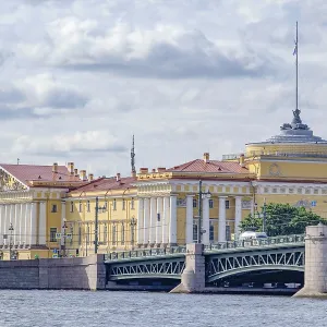Yellow historic building on a river front with bridge and cloudy sky