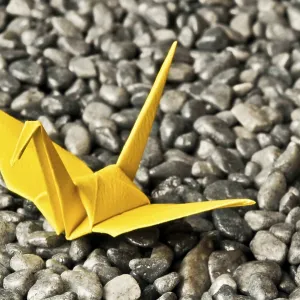 A yellow origami crane sits on a bed of gray pebbles