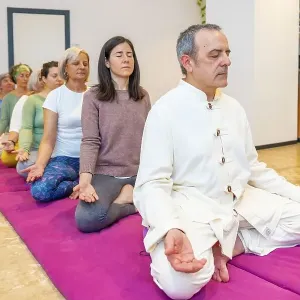 Yoga teacher leading a meditation in a community sitting on mat with lotus position Yoga teacher leading a meditation in a community sitting on mat with lotus position
