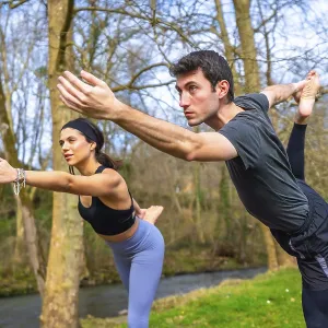 Yoga teachers performing a balancing asana by a river in the forest