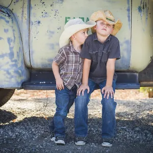 Two young boys wearing cowboy hats leaning against an antique truck in a rustic country setting Two young boys wearing cowboy hats leaning against an antique truck in a rustic country setting