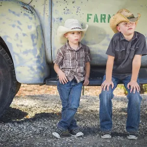 Two young boys wearing cowboy hats leaning against an antique truck in a rustic country setting Two young boys wearing cowboy hats leaning against an antique truck in a rustic country setting