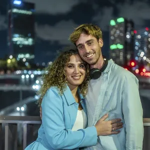 Young couple embracing and smiling at the camera outdoors on a bridge Young couple embracing and smiling at the camera outdoors on a bridge