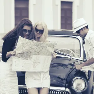 Young fashion people with a road map next to vintage car