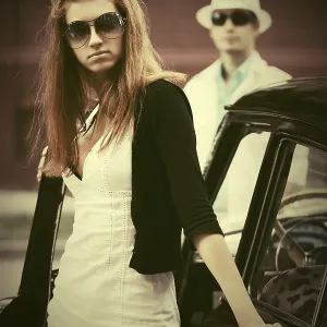 Young fashion woman in sunglasses next to vintage car