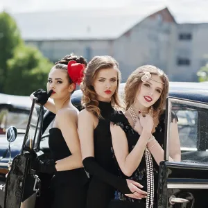 Three young girl in retro style dress near old classic vintage cars
