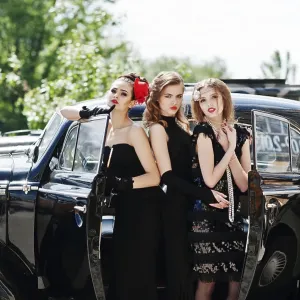 Three young girl in retro style dress near old classic vintage cars
