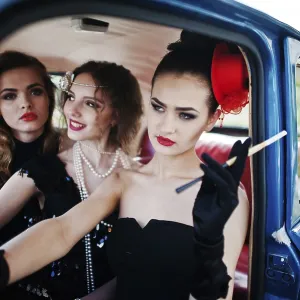 Three young girl in retro style dress seat on old classic vintage car