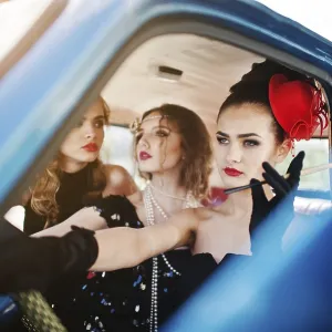 Three young girl in retro style dress seat on old classic vintage car