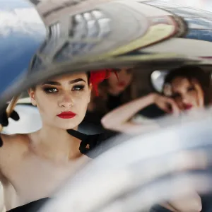 Three young girl in retro style dress seat on old classic vintage car