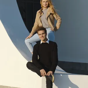 A young man sits on a low wall with his leg bent while a woman stands above him