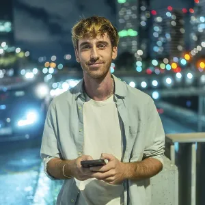 Young man standing outdoors at night smiling at his smartphone Young man standing outdoors at night smiling at his smartphone