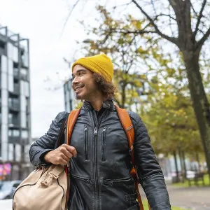 Young man with a yellow beanie and black leather jacket carrying a duffel bag and backpack