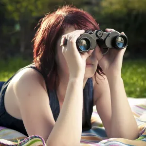 Femme jeune sur un tapis dans une prairie regardant à travers des jumelles.