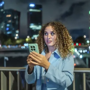 Young woman with curly hair looking surprised while holding a mobile phone Young woman with curly hair looking surprised while holding a mobile phone