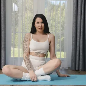 A young woman with dark hair and a tattoo on her arm sits in a yoga pose on a blue mat A young woman with dark hair and a tattoo on her arm sits in a yoga pose on a blue mat