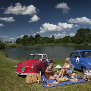 Two young woman having a picnic next to two vintage cars at the lake in sunny weather Two young woman having a picnic next to two vintage cars at the lake in sunny weather
