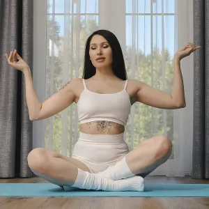 A young woman with long black hair is sitting in a lotus position on a blue yoga mat A young woman with long black hair is sitting in a lotus position on a blue yoga mat