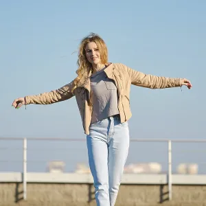 A young woman with long, flowing hair strides across a rooftop terrace on a clear