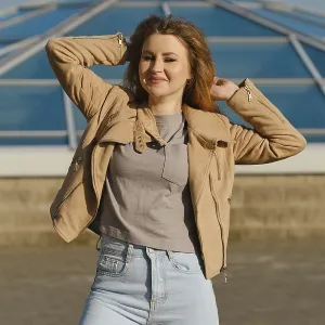 Young woman poses confidently in casual outfit against modern glass structure on sunny day