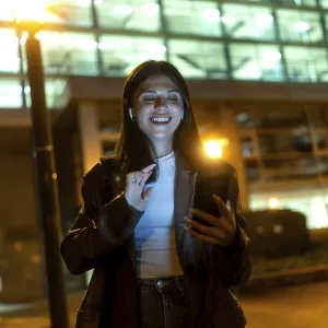 Young woman smiling broadly, wearing wireless earbuds and dark jacket Young woman smiling broadly, wearing wireless earbuds and dark jacket