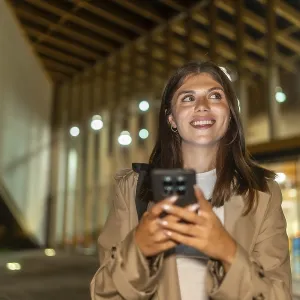 Young woman smiling while holding a smartphone and looking up Young woman smiling while holding a smartphone and looking up