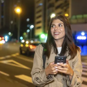 Young woman smiling and looking away while using a mobile phone on a pedestrian crossing Young woman smiling and looking away while using a mobile phone on a pedestrian crossing