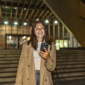 Young woman smiling while looking at her mobile phone outdoors Young woman smiling while looking at her mobile phone outdoors