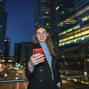 Young woman smiling while reading content on her red smartphone Young woman smiling while reading content on her red smartphone