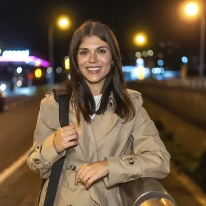 Young woman smiling while standing in a trench coat on an urban street at night Young woman smiling while standing in a trench coat on an urban street at night