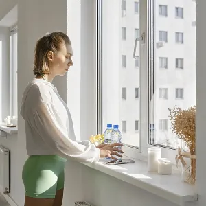 A young woman stands by a large window A young woman stands by a large window