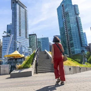 Young woman tourist walking up stairs in a modern city park with skyscrapers