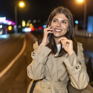 Young woman in a trench coat smiling happily while having a phone call Young woman in a trench coat smiling happily while having a phone call