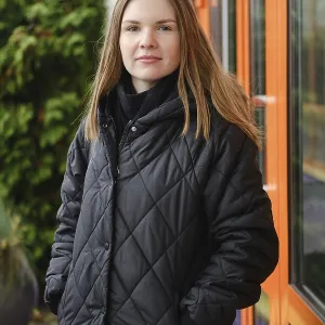 A young woman wearing a black quilted coat stands confidently outside a building