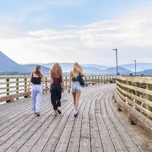 Three young women are enjoying a leisurely stroll along a scenic wooden pier in salmon arm Three young women are enjoying a leisurely stroll along a scenic wooden pier in salmon arm
