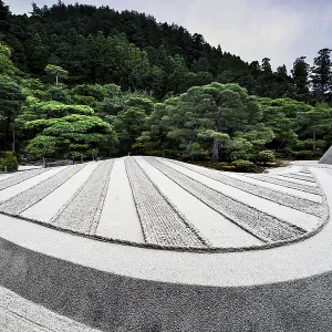 Zen garden of Ginkaku-ji Temple with precise sand patterns and rocks surrounded by green landscape Zen garden of Ginkaku-ji Temple with precise sand patterns and rocks surrounded by green landscape