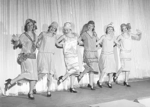 1920s remake. A group of women at a theatre are posing on stage in typical 1920s dresses and hats