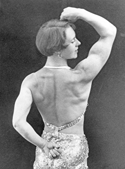 In the 1930s. A woman pictured from behind when she demonstrates her fit body and muscles. A bit of a stage costume is visible