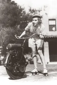 In the 1930s. A woman on roller skates holds on the handlebars of a one-wheel motorcycle that pulls her forward. She looks focused when the speed picks up
