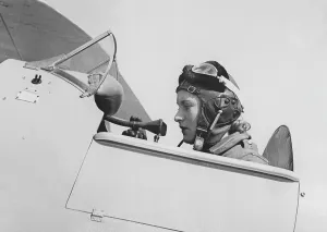 In the 1930s. A young female pilot is seen sitting in the cockpit of her airplane wearing the leather cap