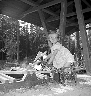1940s girl. A little girl with her tricycle is having some difficulty when trying to get it out of the bicycle stand